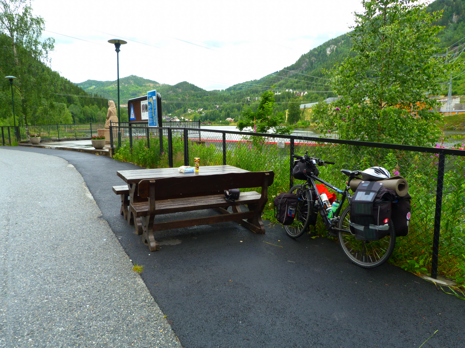 Fahrrad in Norwegen, an Gerüst lehnend. Zu sehen eine Bank, Berge und viel grün