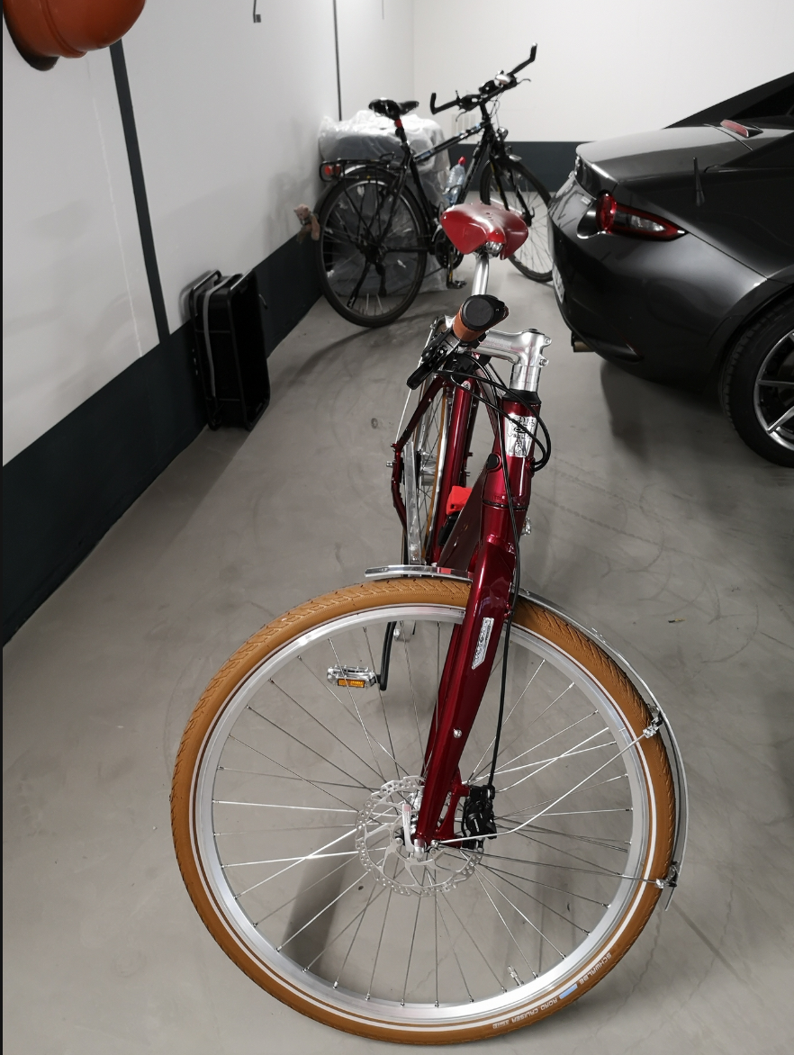 Rotes Fahrrad im Vordergrund, Schwarzes im Hintergrund, Kofferraum von Auto zu erkennen