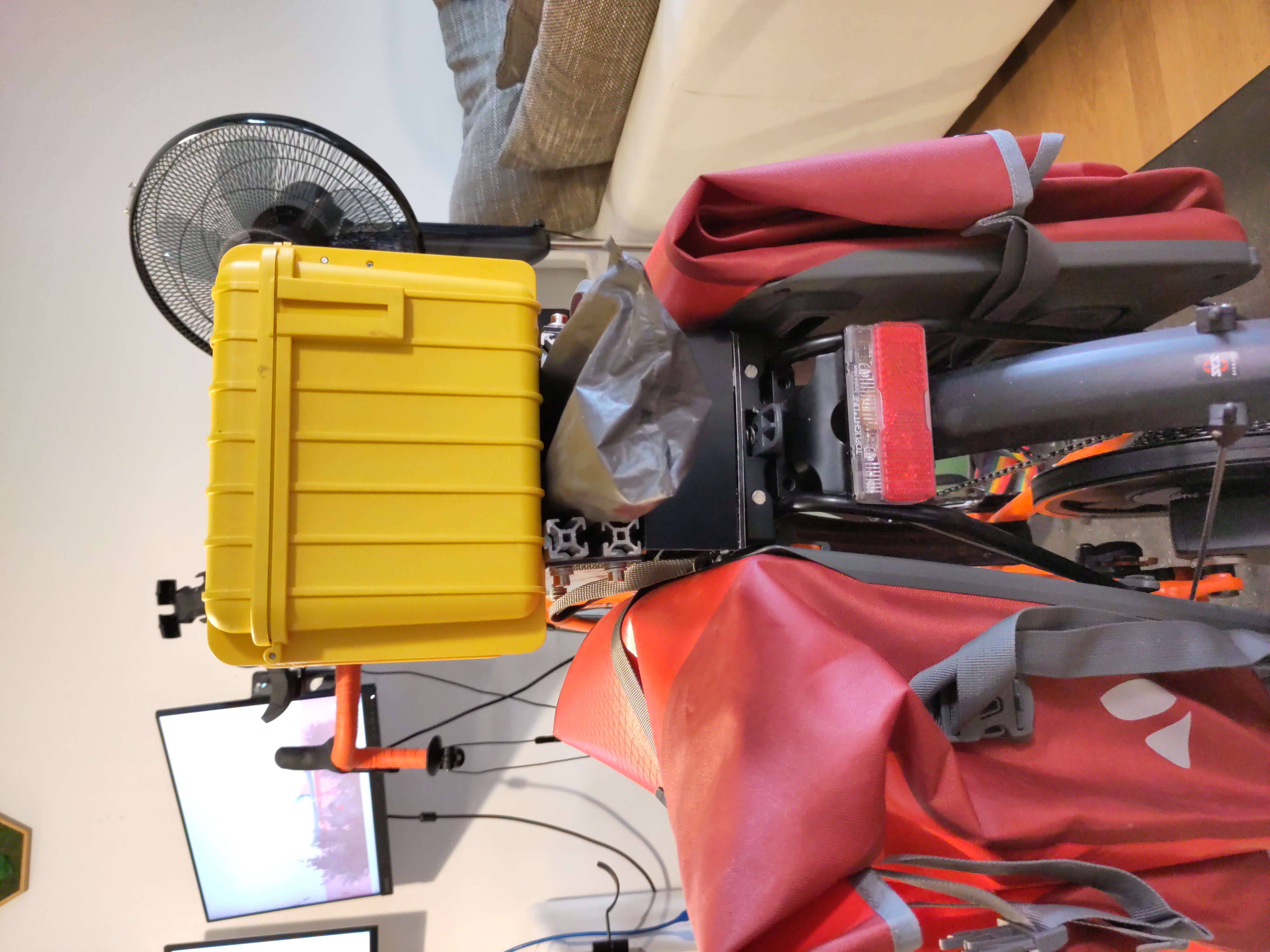 Fahrrad von Hinten. Gelbe Kiste und Zeltstangen auf dem Gepäckträger